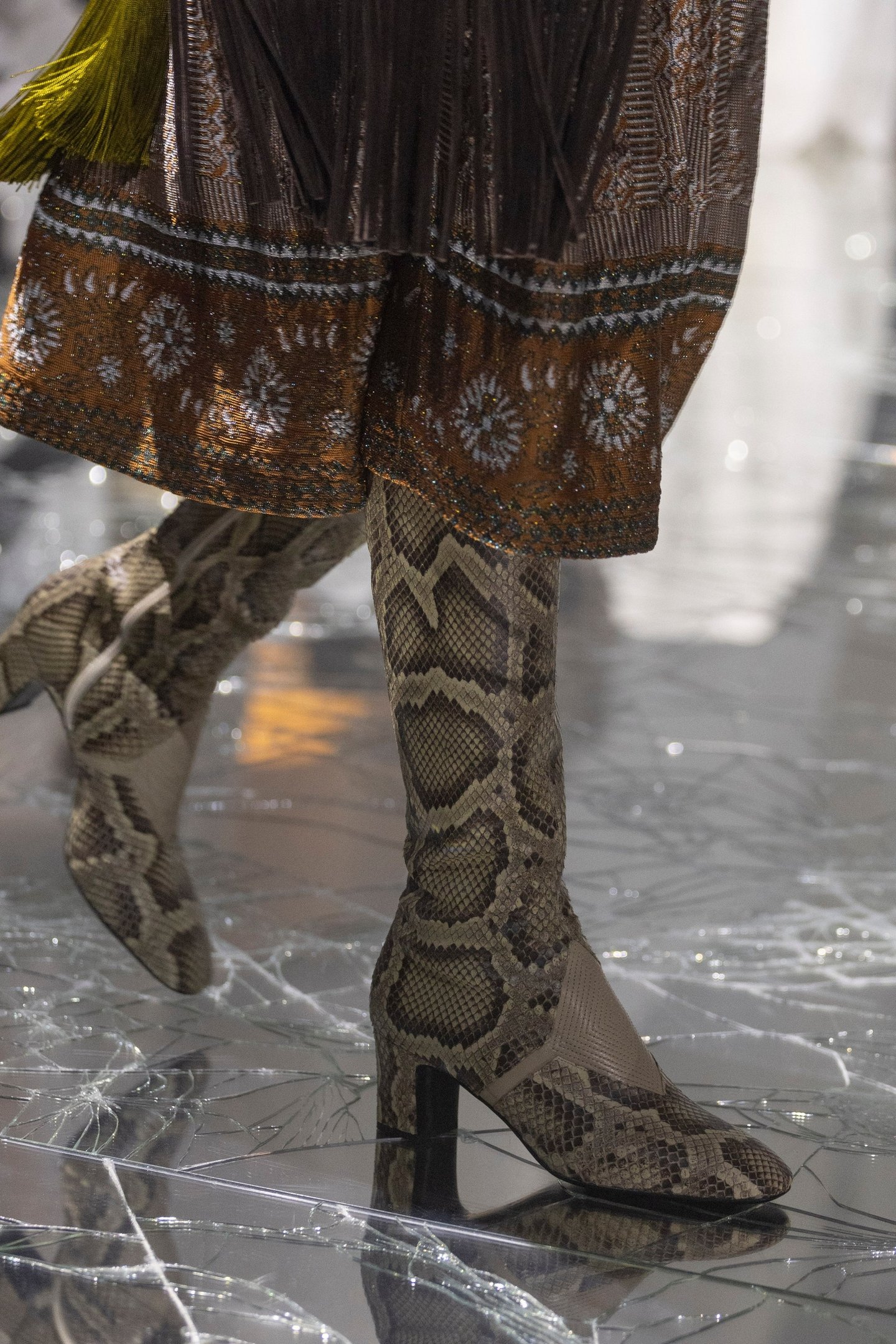 Botas de cano alto com estampa de cobra combinadas com um vestido de padrão geométrico em tons terrosos.