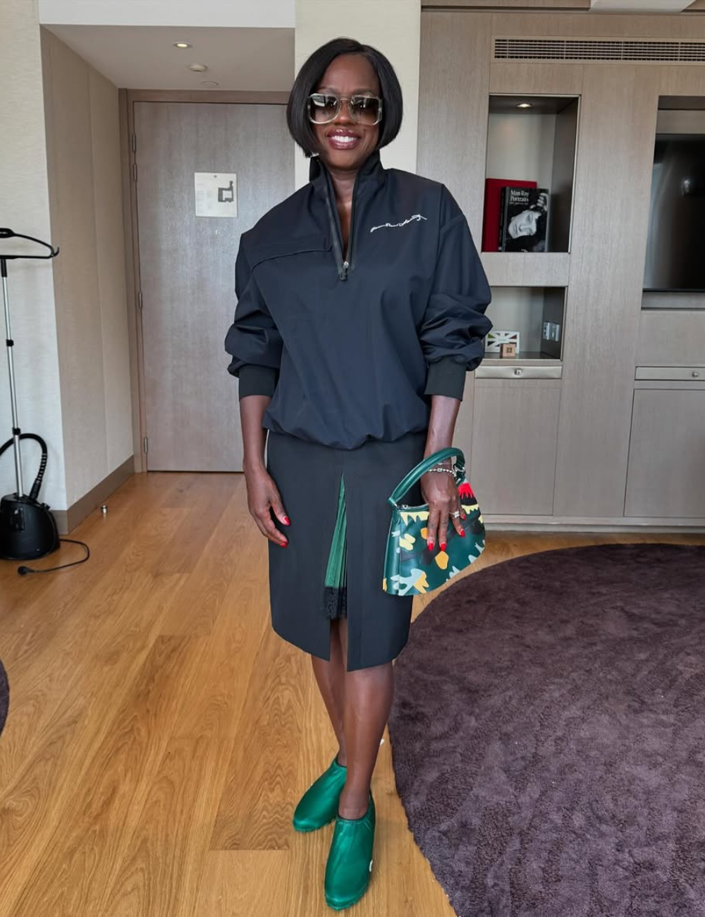 A mulher está em ambiente elegante, vestindo roupa escura com bolsa colorida.