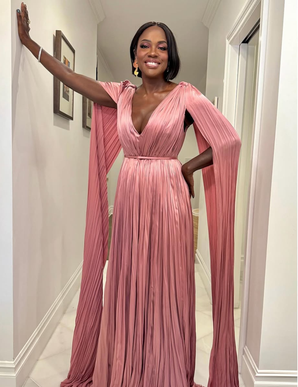 Viola Davis está usando um vestido longo e rosa, posando em um corredor.