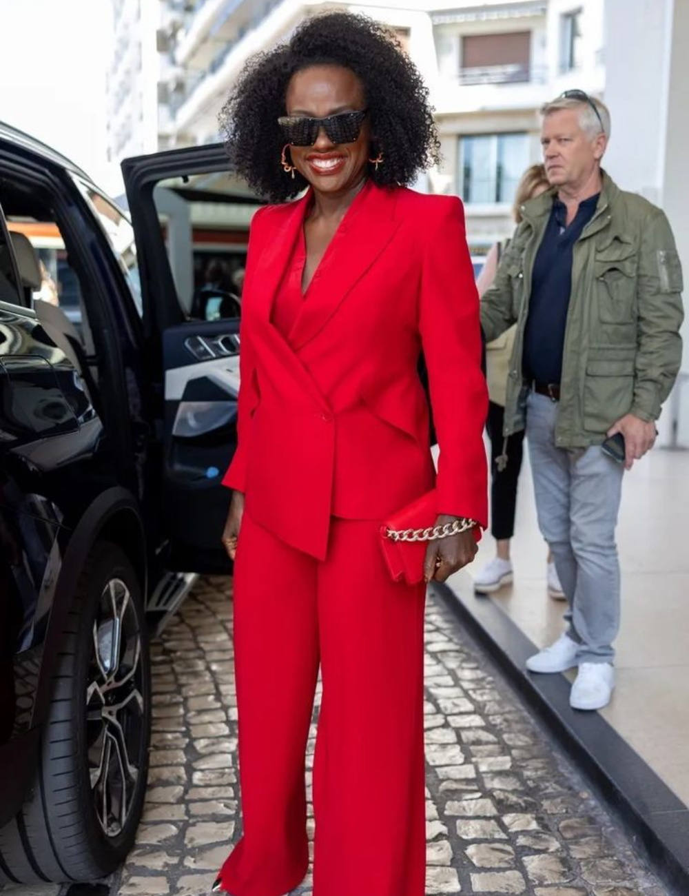 Viola Davis usando um terno vermelho e óculos escuros está saindo de um carro, sorrindo.