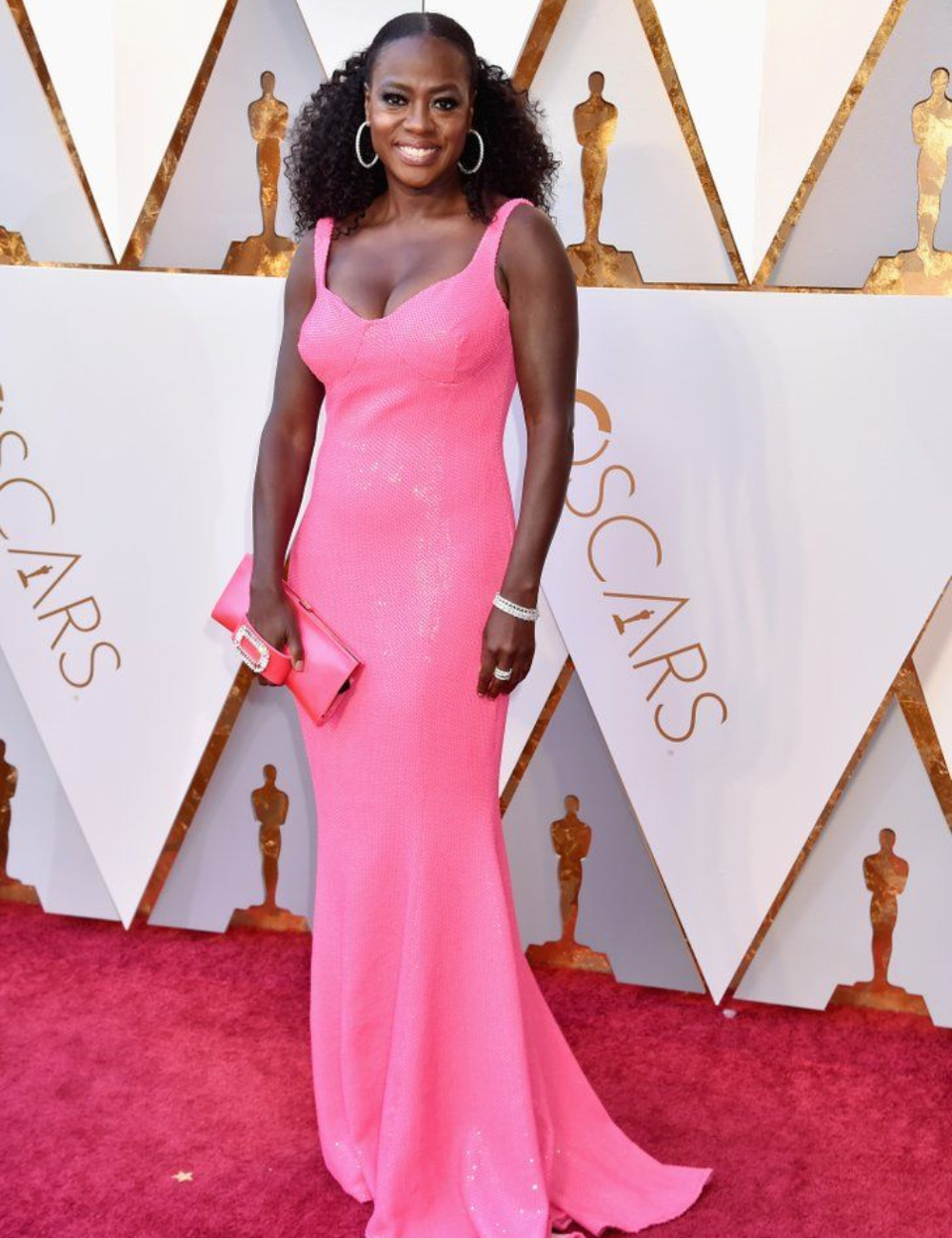 Viola Davis usando um vestido longo rosa, posando sorrindo em frente ao mural do Oscar.