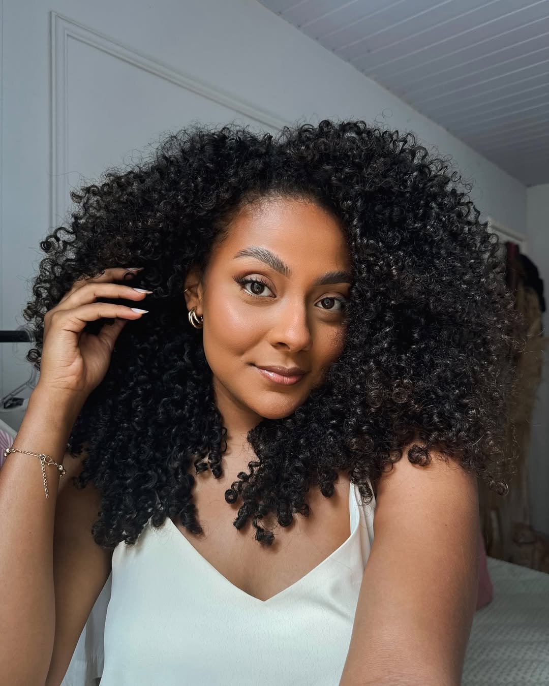 Mulher com cabelo cacheado volumoso e vestido branco, exemplificando cuidados do guia do cabelo cacheado.