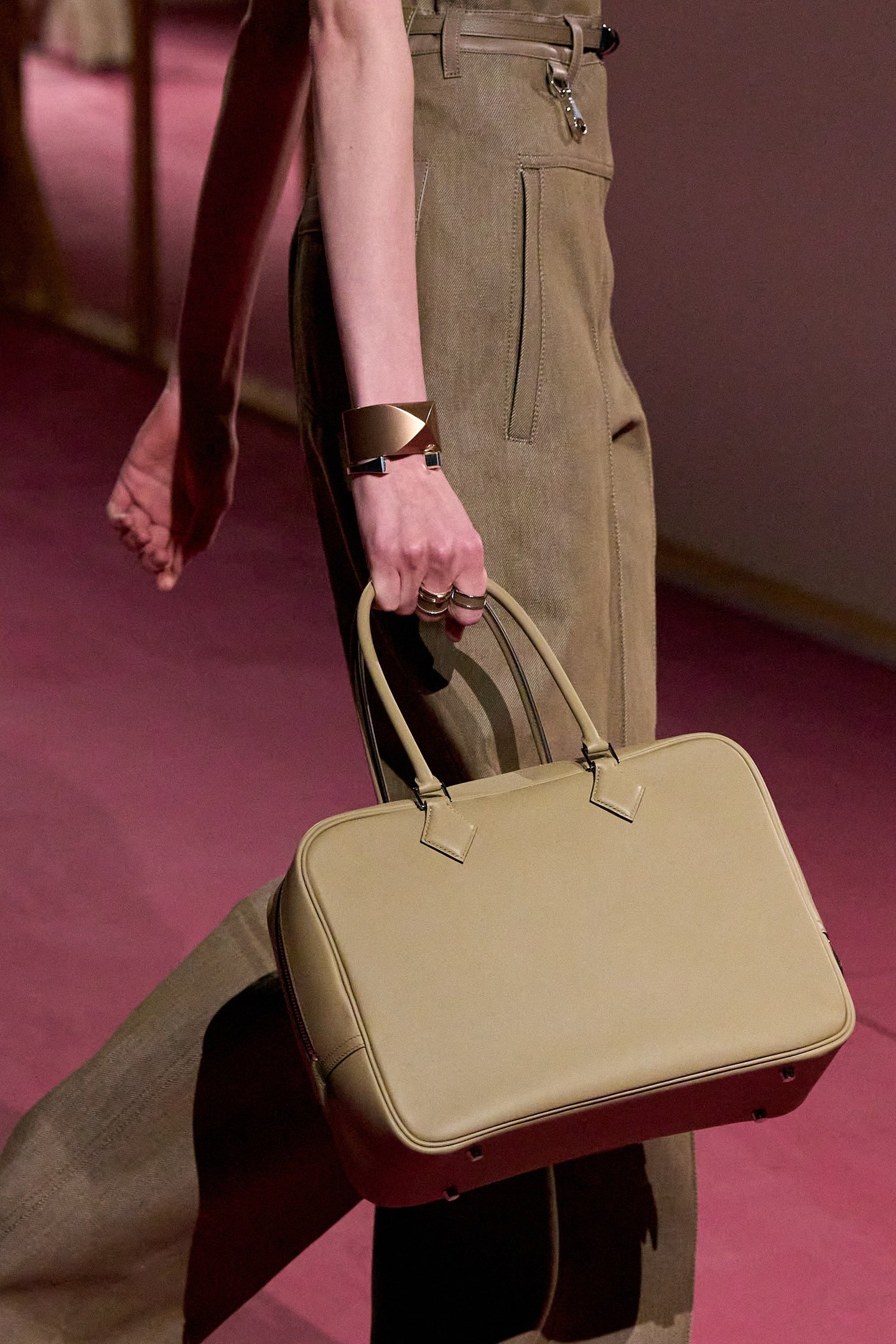 Pessoa segurando uma bolsa bege estilo doctor bags, usando calças de tecido bege e pulseira moderna.
