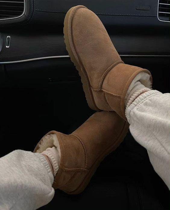 Botas marrons de camurça e lã, típicas da história da UGG, usadas com calça clara em um carro.