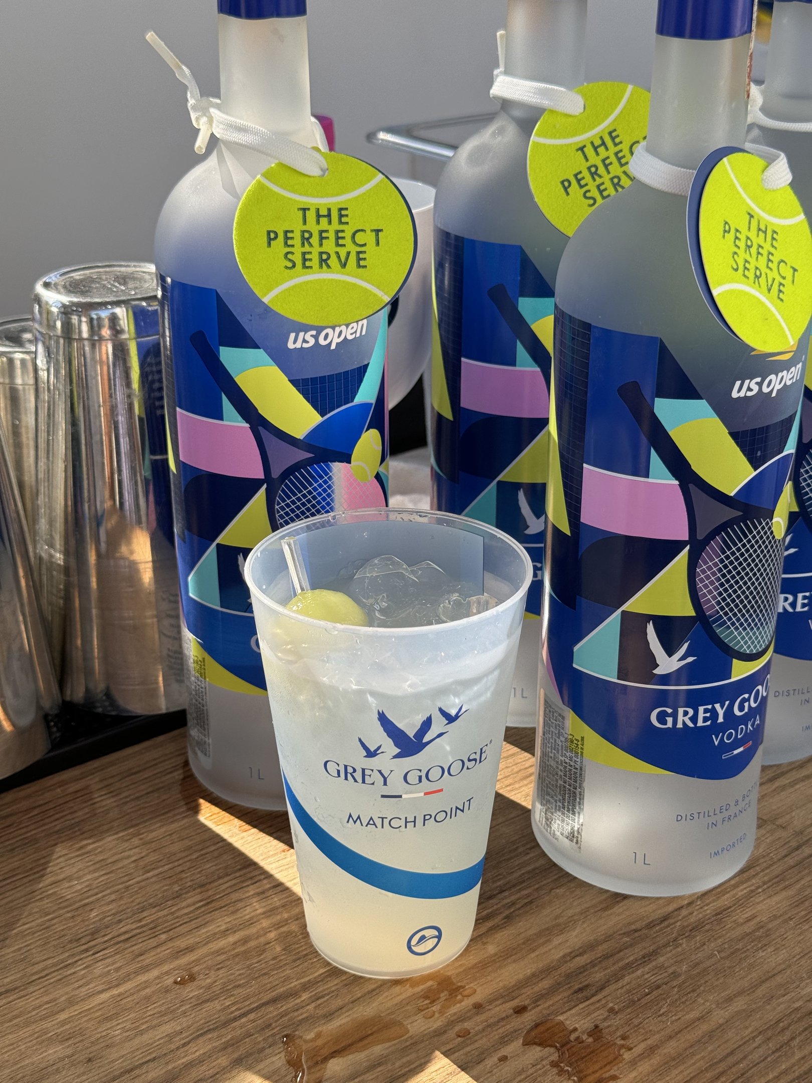 Copos e garrafas de vodca Grey Goose expostas em uma mesa, destacando evento esportivo. Rio Open não é mencionado.