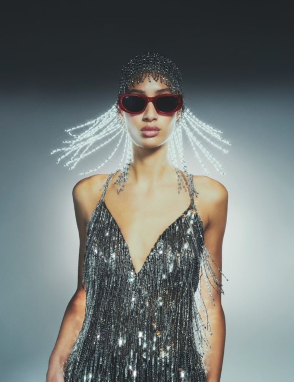 Modelo em vestido prateado cintilante com óculos escuros e adereços na cabeça, ilustrando lançamentos de moda mais estilosos.
