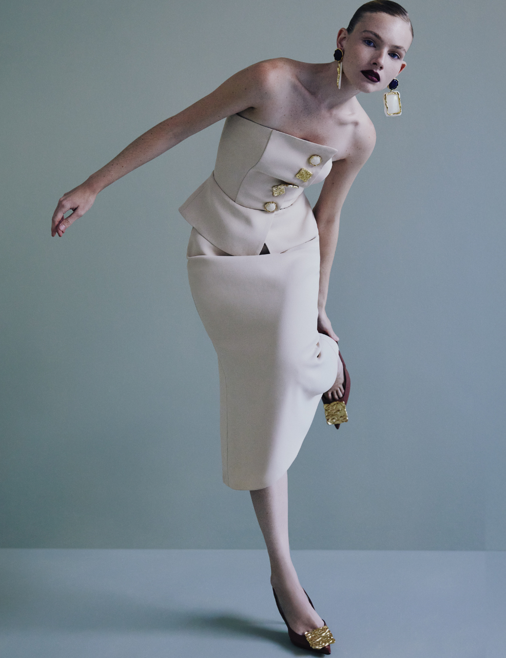 Modelo vestindo conjunto elegante em tom nude, com botões dourados, sapatos e acessórios marcantes. Destaque em lançamentos de moda mais estilosos.