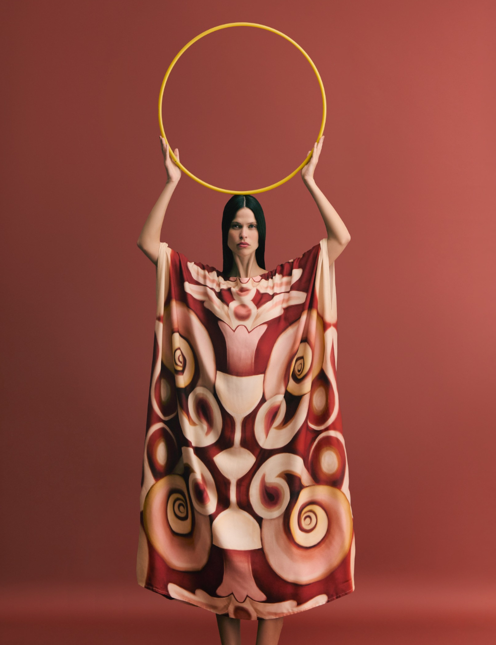 Modelo em capa estampada, segurando um aro amarelo. Lançamentos de moda destacados pelo design ousado.