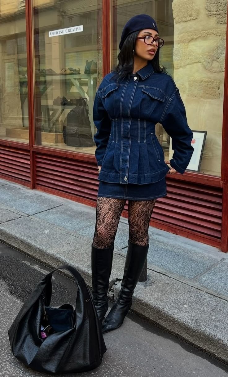 Pessoa usando casaco de jeans, minissaia, meias rendadas e botas longas. Bolsa preta no chão. Look all jeans.