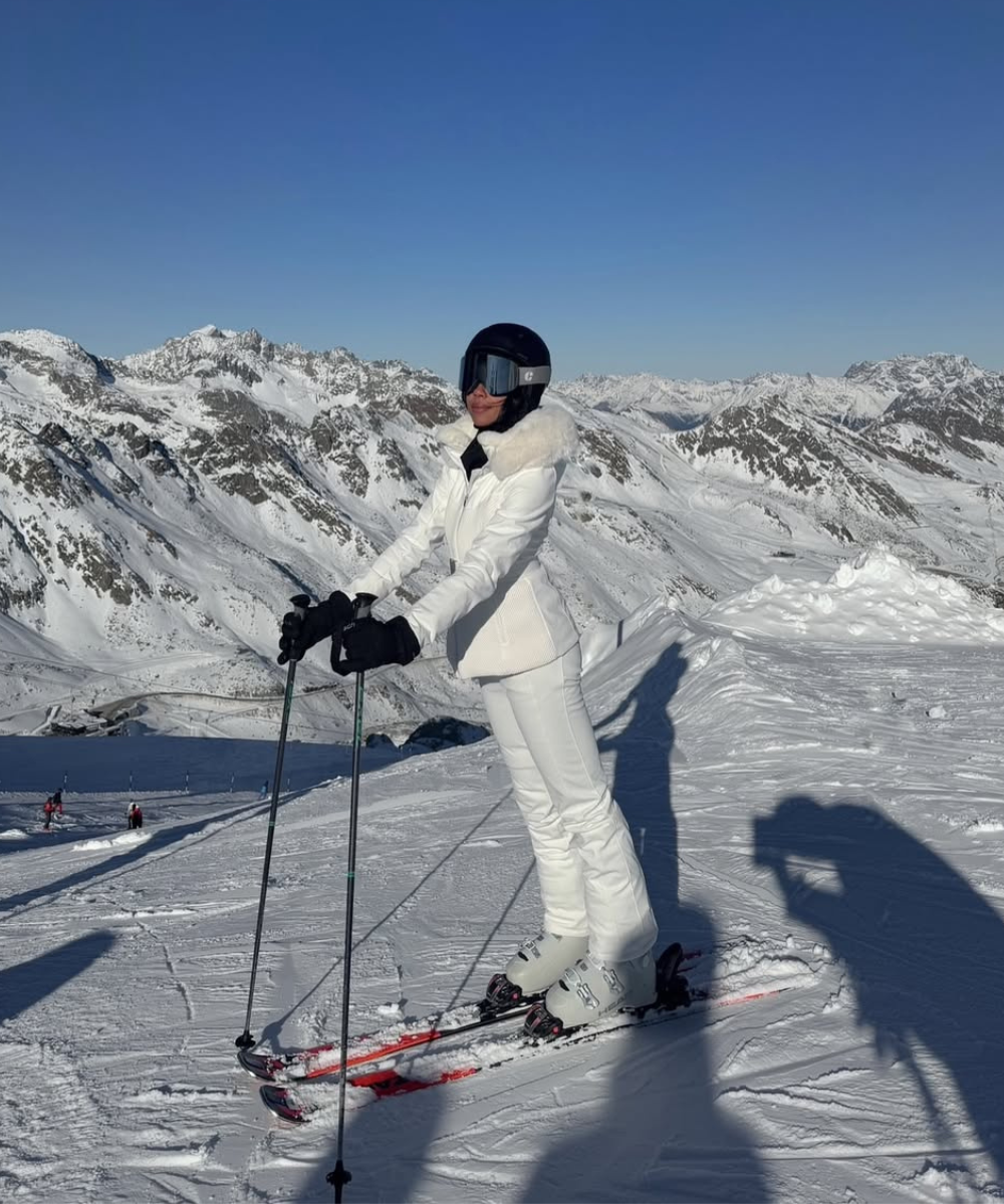 Esquiadora com roupa branca em montanha nevada, exibe looks estilosos para esquiar.