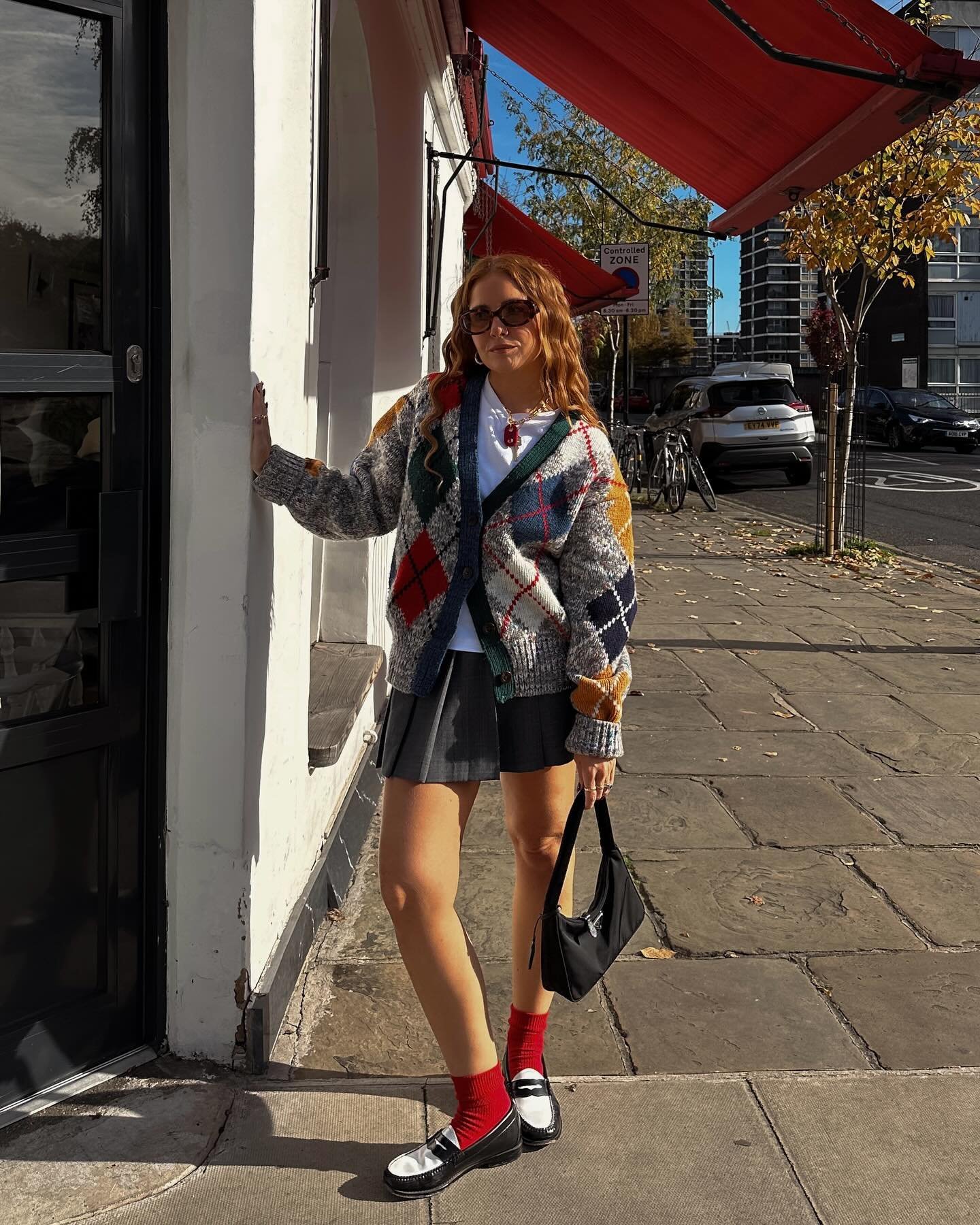 Cardigan de padronagem xadrez colorido com saia plissada e sapatos pretos. Estilo casual urbano.