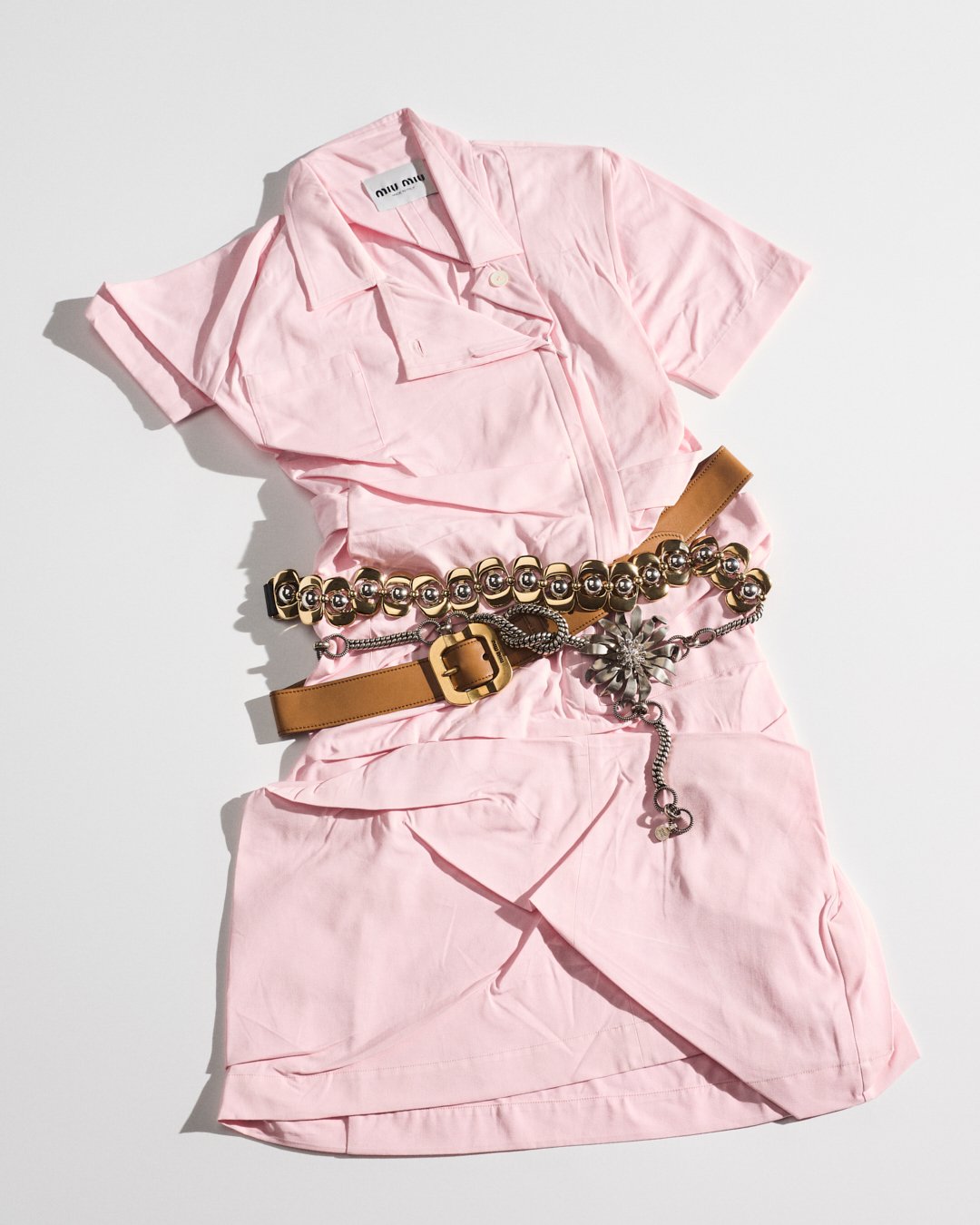 Vestido rosa com cinto decorativo marrom e dourado, evocando um estilo loud luxury.