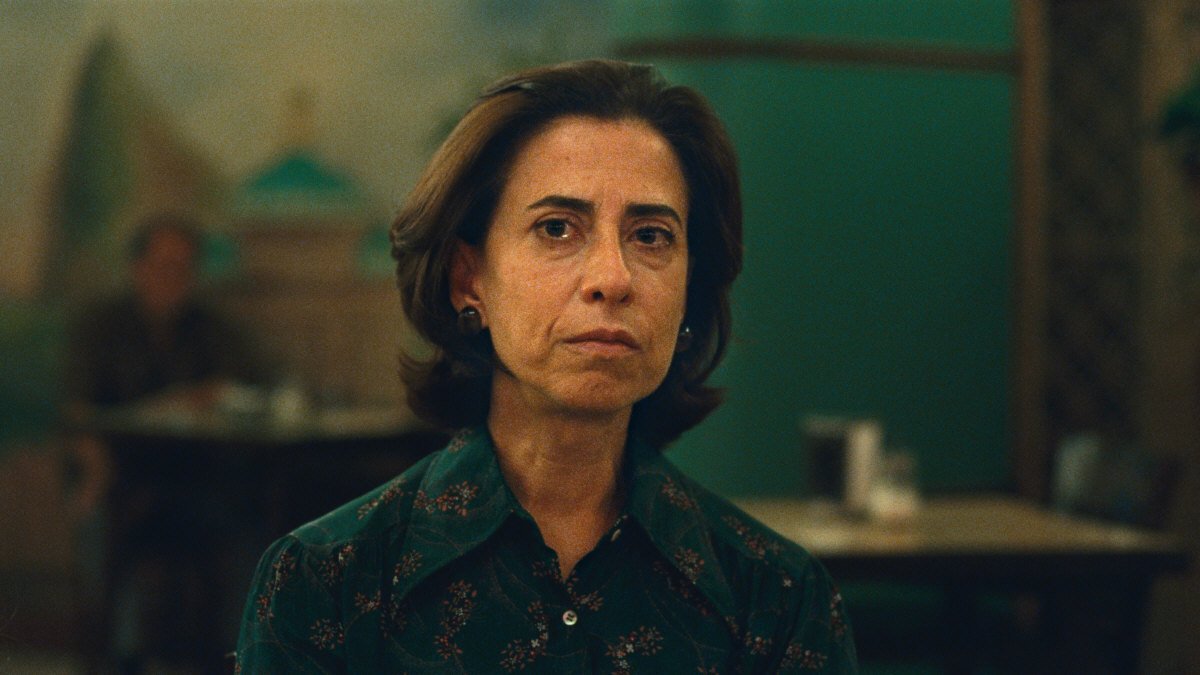 Mulher em ambiente interno, com expressão séria. Maquiagem no cinema realça traços faciais discretamente. Fundo desfocado.