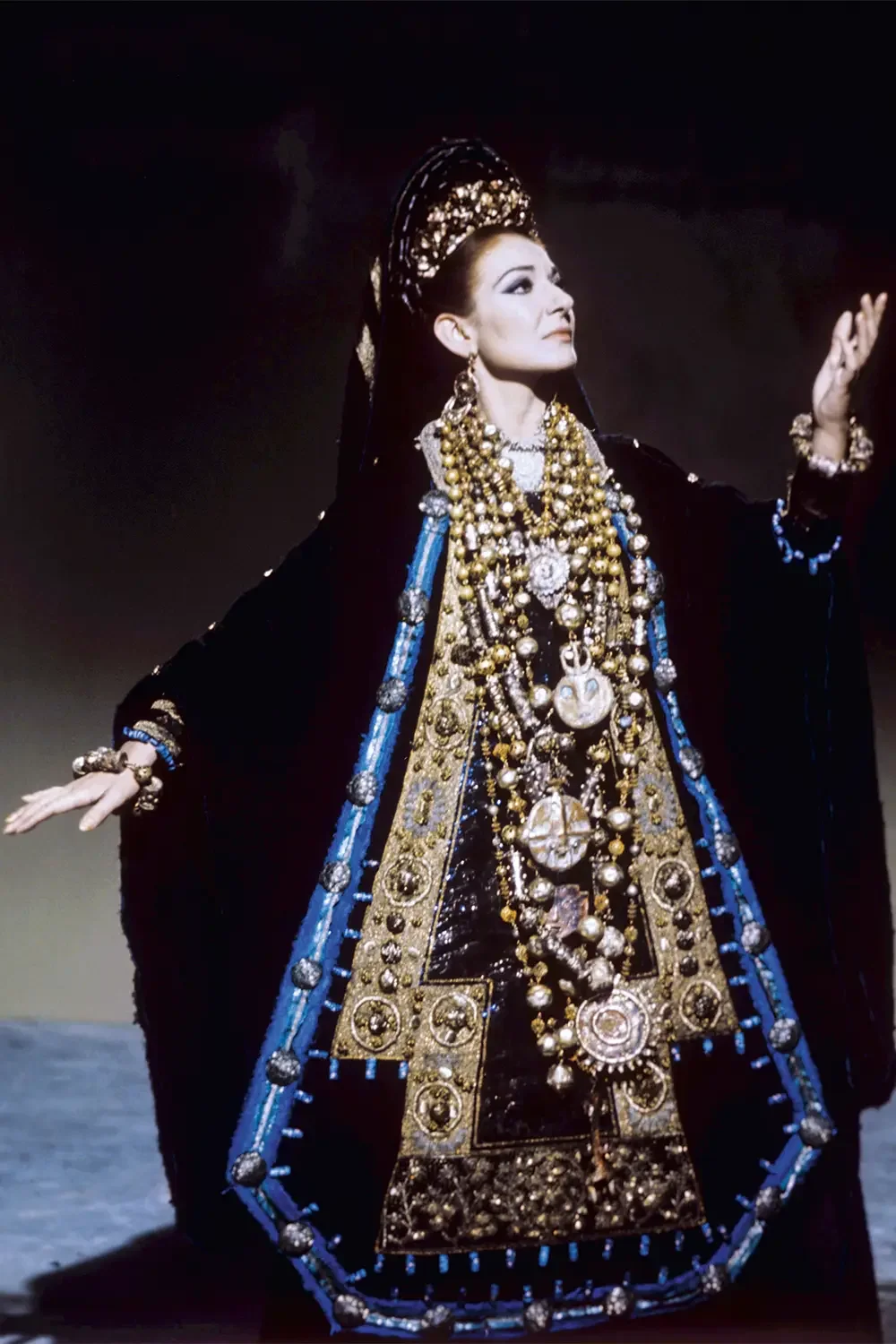Maria Callas usando um traje reluzente com detalhes decorativos dourados e azuis.