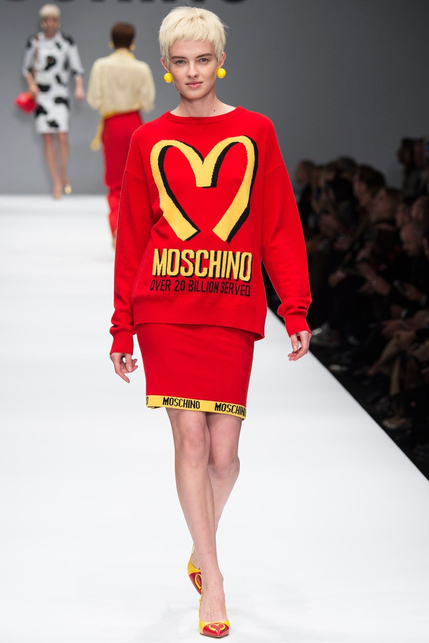 Modelo com roupa vermelha inspirada em fast food, desfilando em passarela de moda.