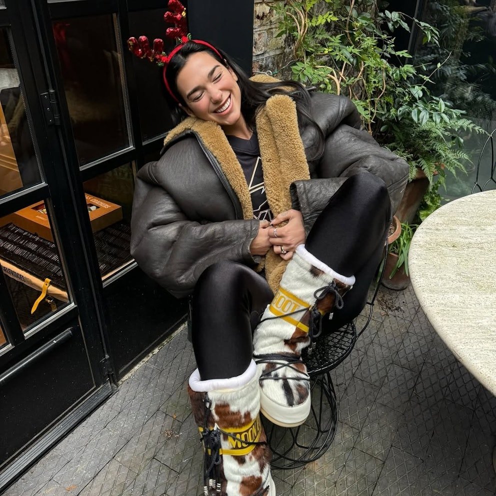 Pessoa sorrindo, usando casaco de pele falsa e acessórios natalinos. Sapatos tipo moon boot brancos com padrão animal.