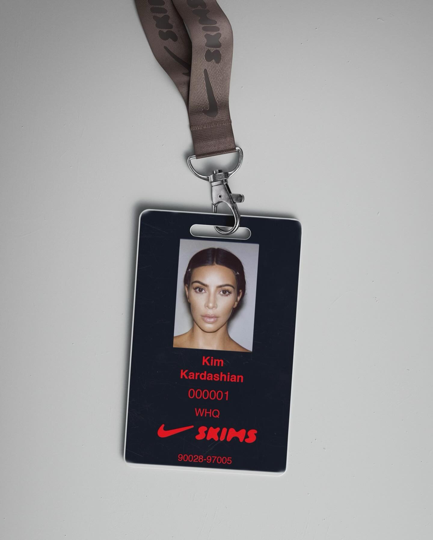 Crachá com foto de kim Kardashian, acompanhado de cordão marrom com logotipo. Texto em vermelho inclui