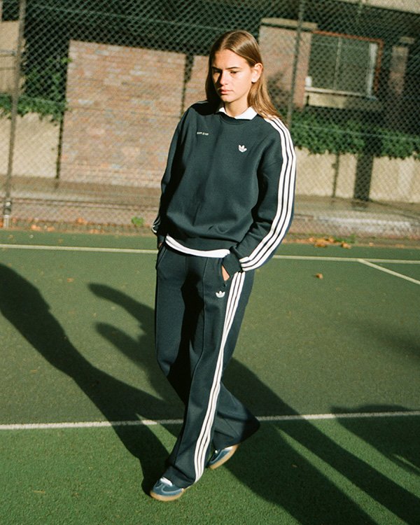 Pessoa em conjunto esportivo preto com listras Adidas Originals e Sporty & Rich.