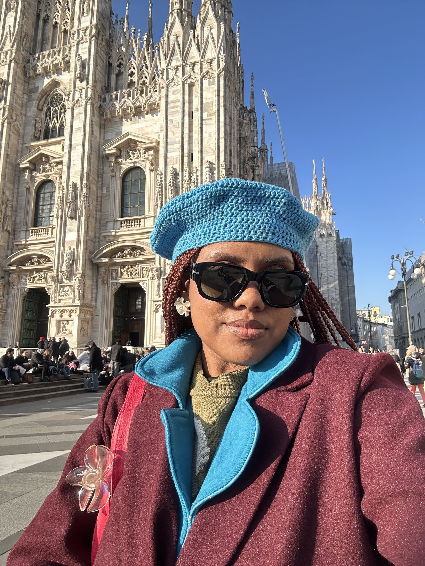 Pessoa com boina azul e casaco vinho em frente a uma catedral gótica na luz do dia. Ocupar espaços