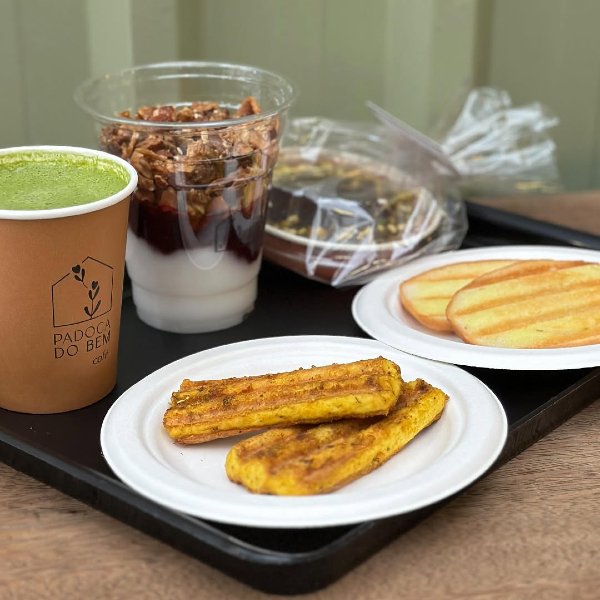Biscoitos e barrinhas de milho acompanham uma bebida verde e iogurte com granola, destacando produtos sem glúten.