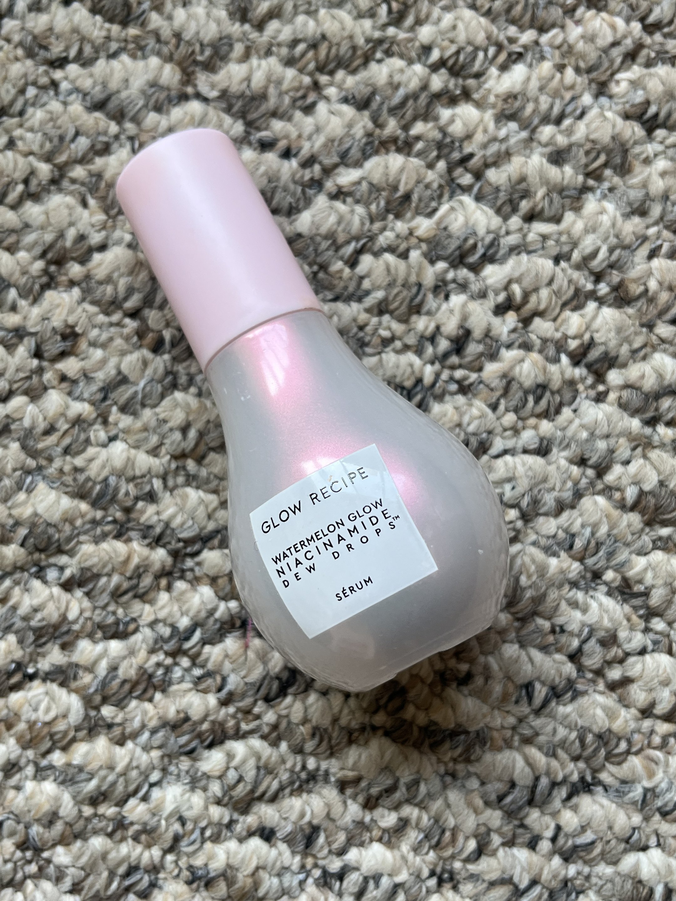 Sérum Watermelon Glow Niacinamide Dew Drops da produtos da Glow Recipe sobre um tapete texturizado.