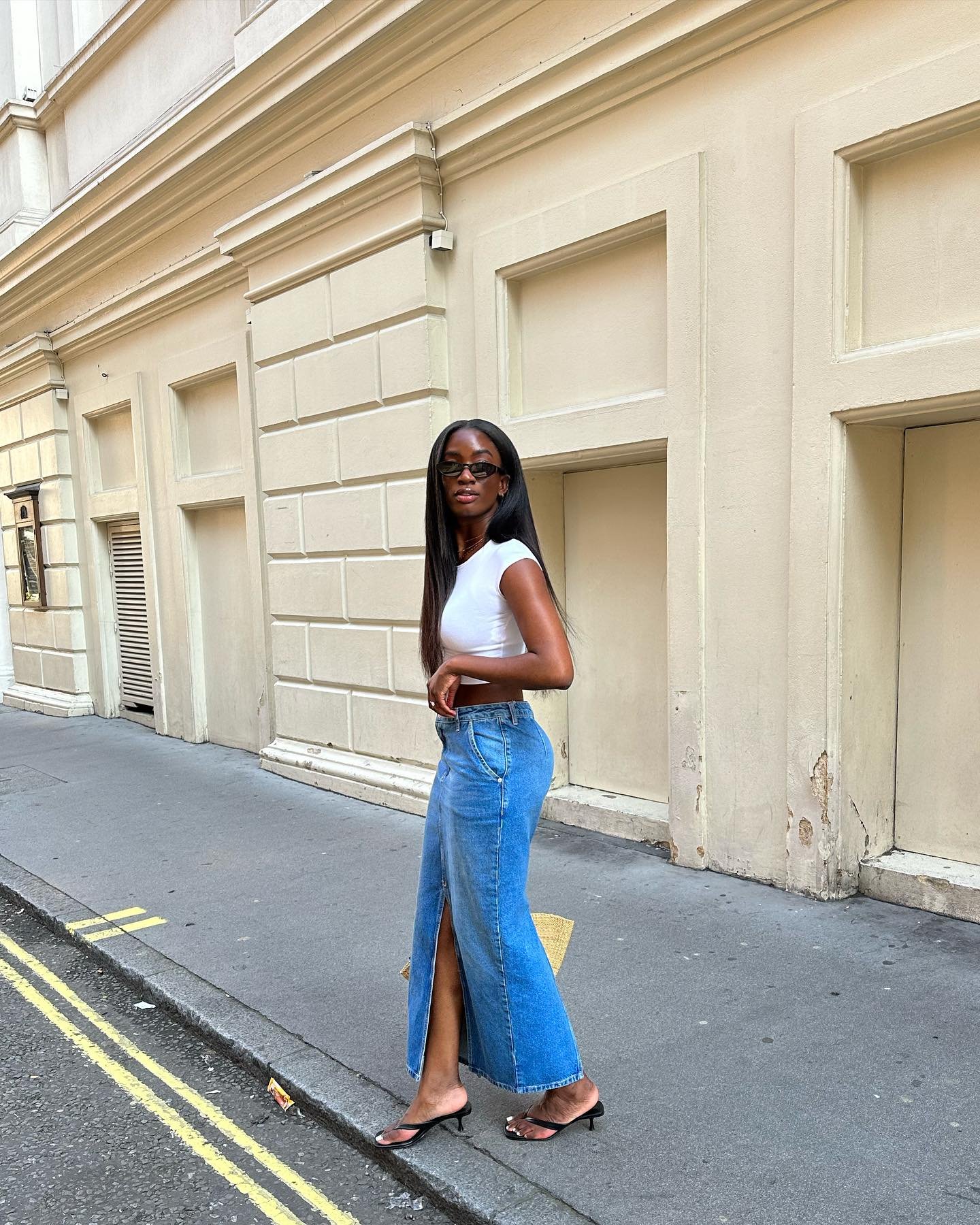 Mulher com saia jeans e top branco caminha em rua urbana, usando sapatos retrô de salto.