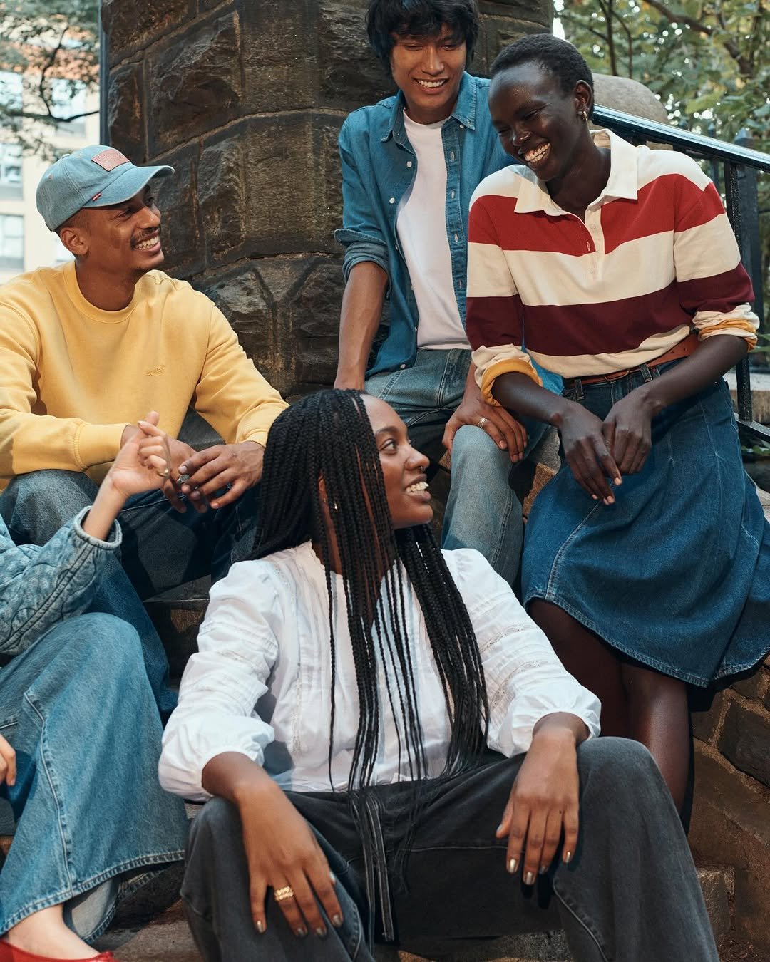 Grupo diverso de amigos sorrindo e conversando em escadas ao ar livre, destacando amizade e conexão usando jeans oversized 