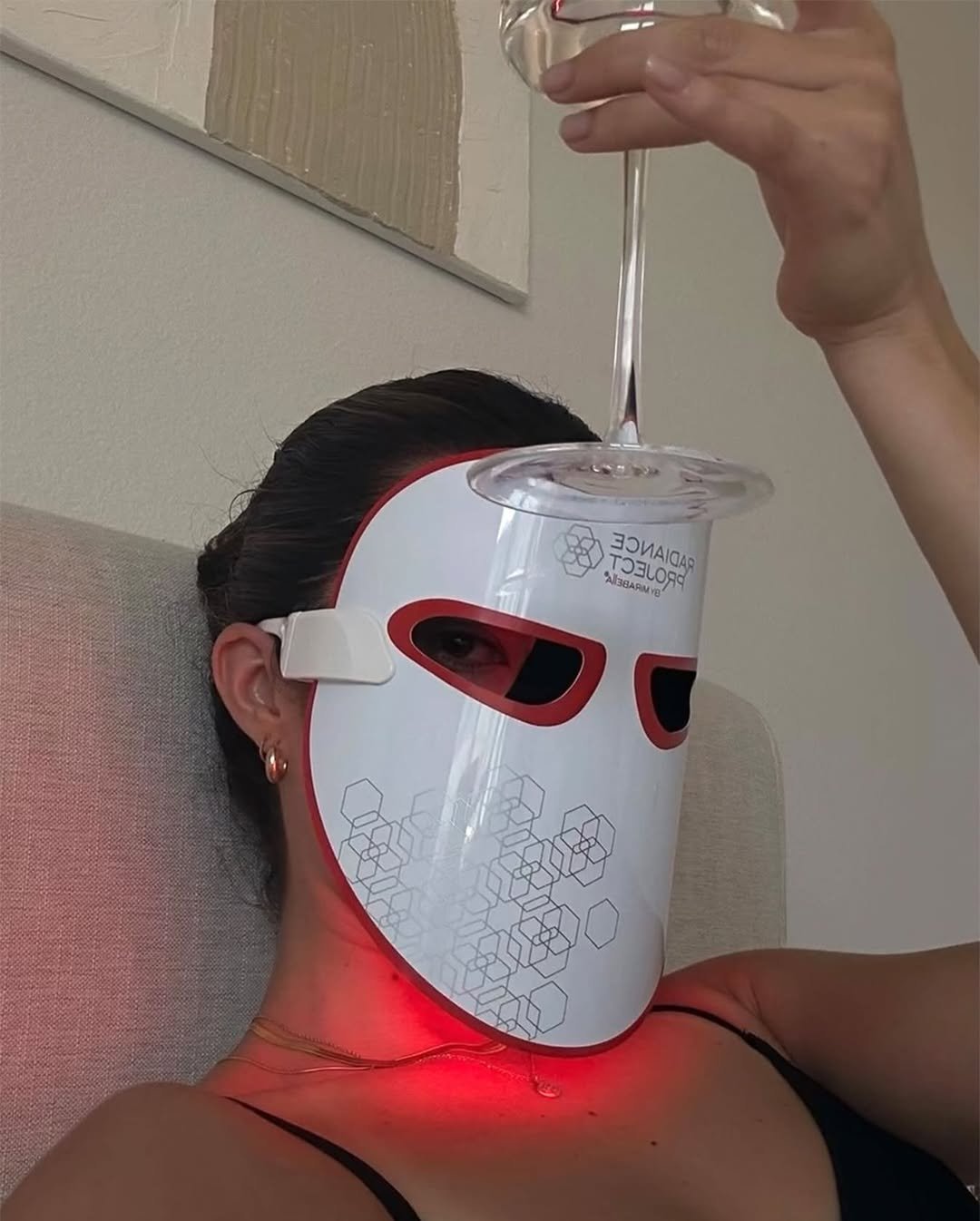 Máscara facial LED inovadora usada em tendências de maquiagem para 2025, pessoa segura uma taça.