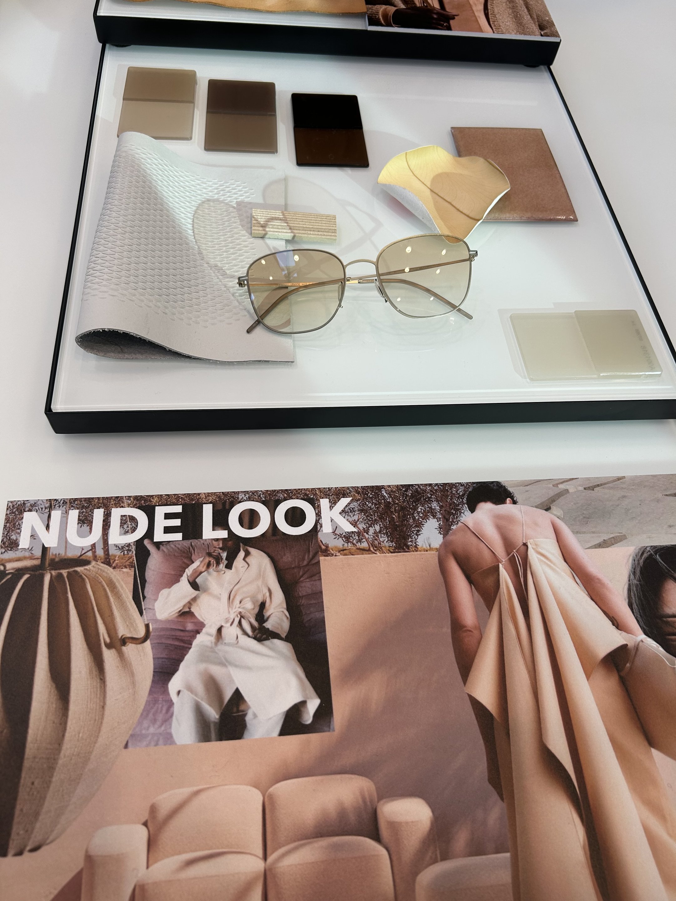 Óculos de armação metálica em display com amostras de tecido e cores neutras, refletindo tendências de óculos.