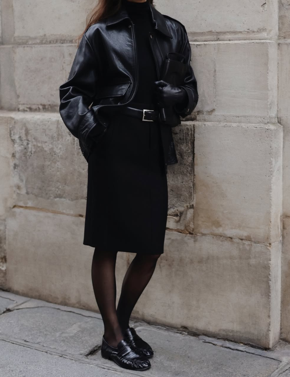 Pessoa usando casaco de couro preto com saia e luvas, estilo elegante influenciado por tendências vintage.