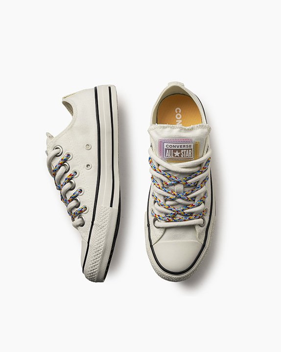 Tênis brancos Converse All Star com cadarços coloridos, um visto de cima e outro de lado.