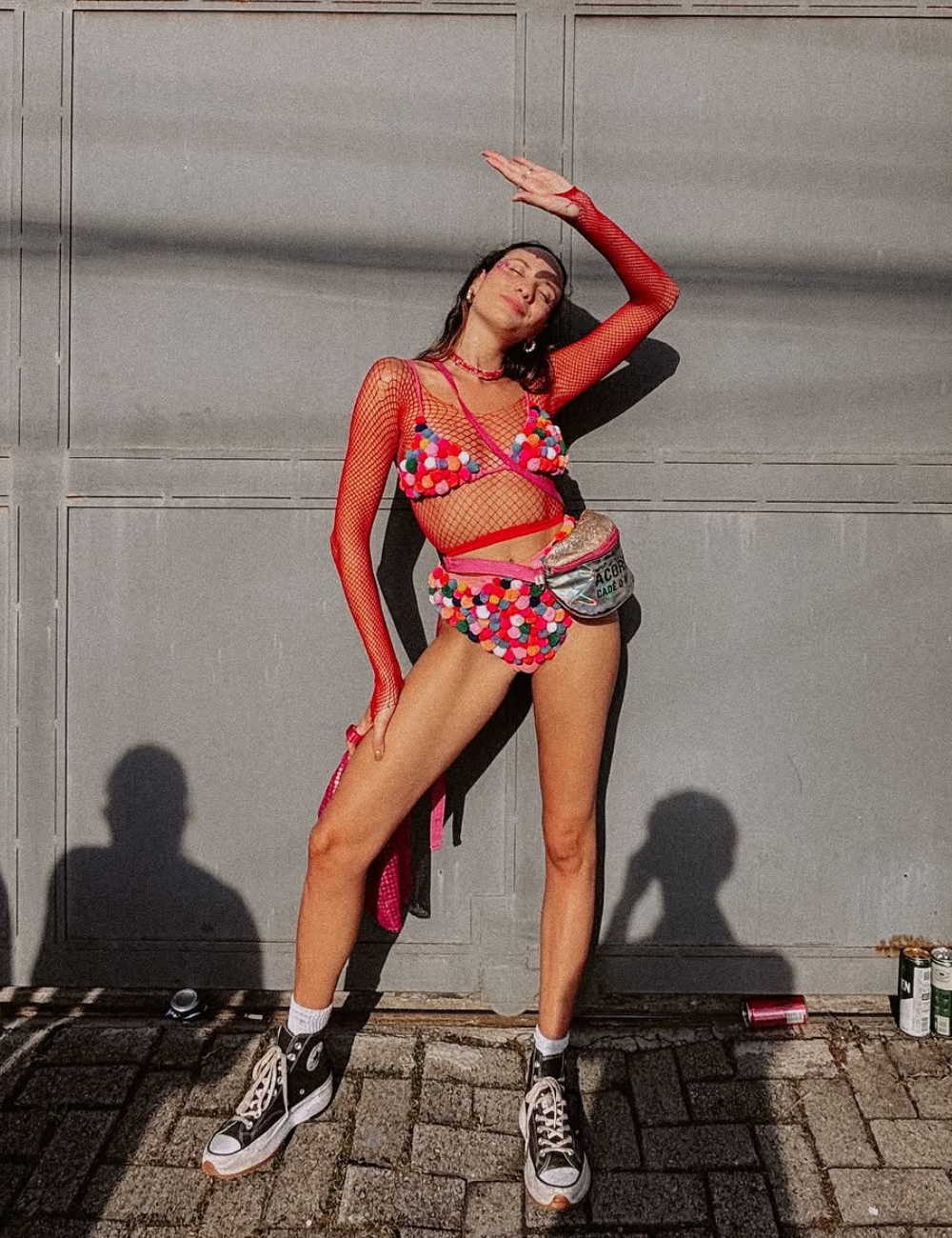 Mulher em traje colorido com o tênis para o Carnaval perfeito, posando em frente a uma parede cinza.