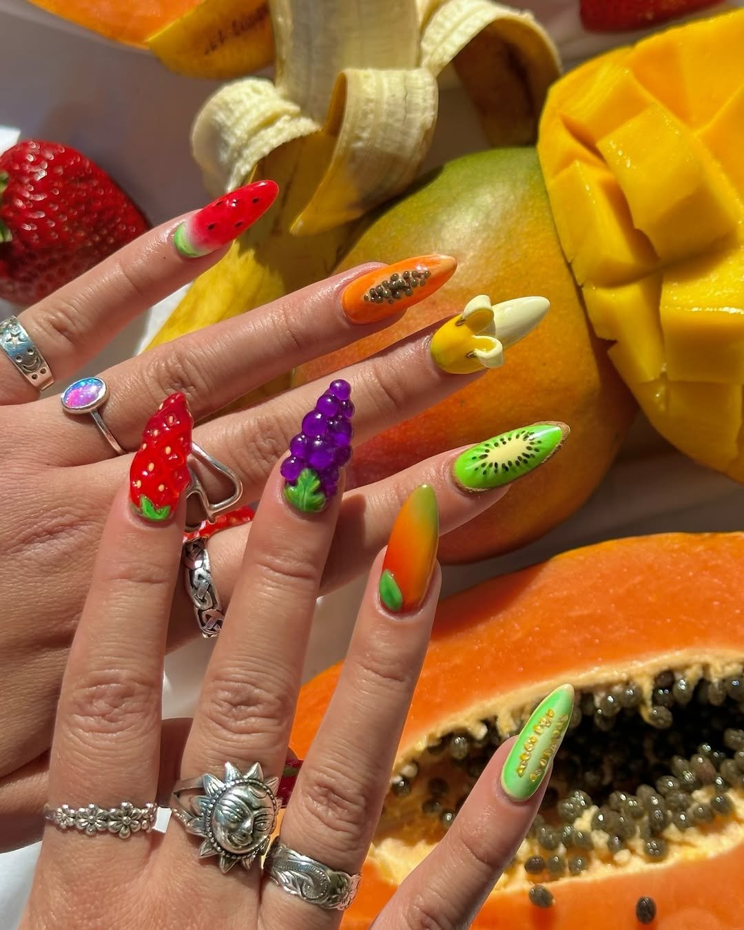 Unhas decoradas em 3D com designs de frutas variadas, incluindo melancia, uva, kiwi e morango.