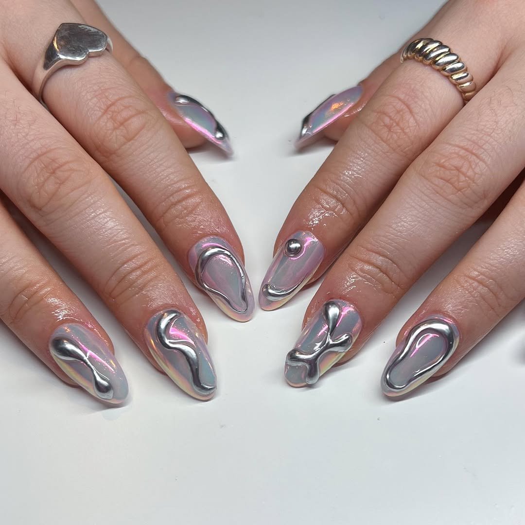 Mãos com unhas 3D em design prateado e rosa metálico, criando efeito futurista.