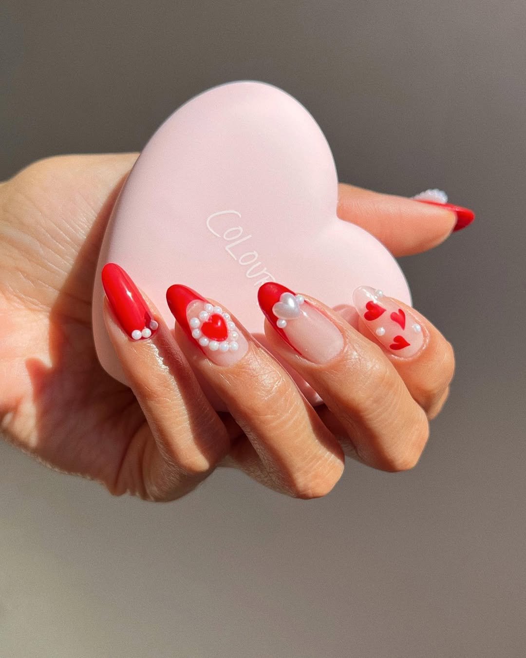 Unhas 3D com decoração de corações vermelhos e pérolas em detalhes. Mão segura objeto em forma de coração.