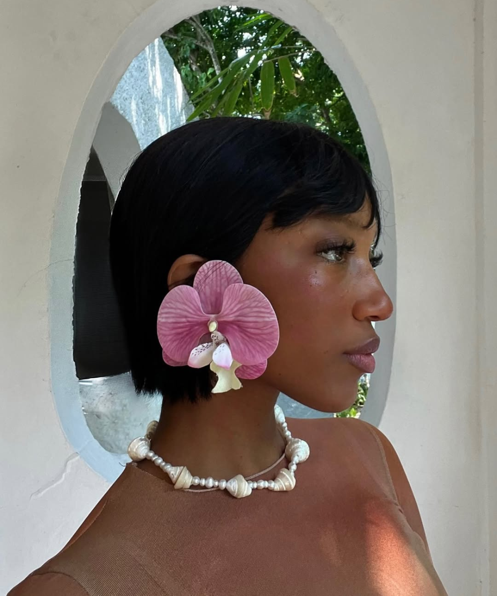 Jovem com brinco de flor rosa e colar de conchas, evocando o verão em Ibiza.
