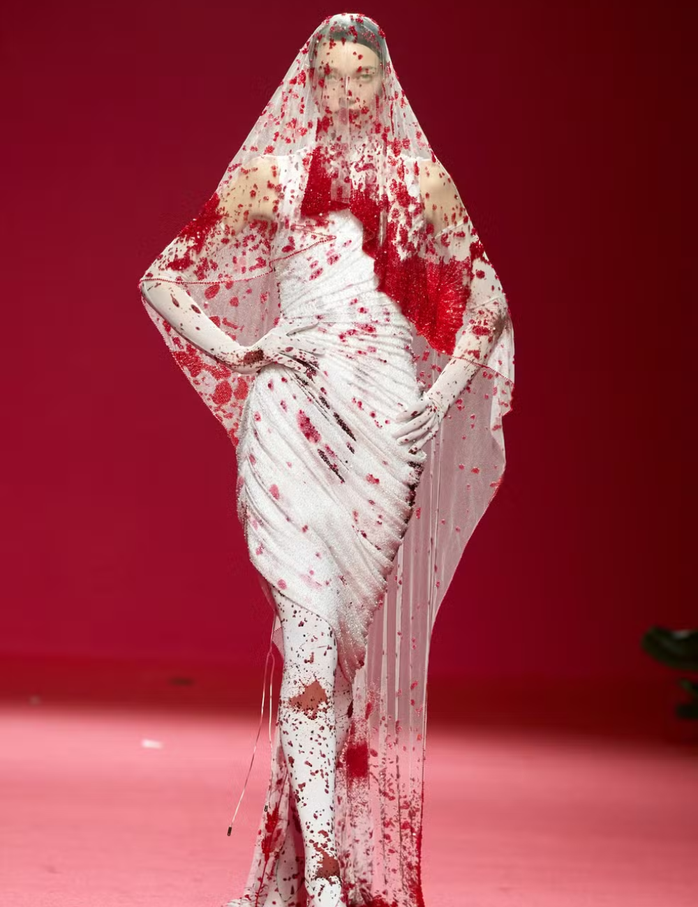 Vestido de noiva da alta-costura branco com detalhes em vermelho sobre um fundo vermelho.