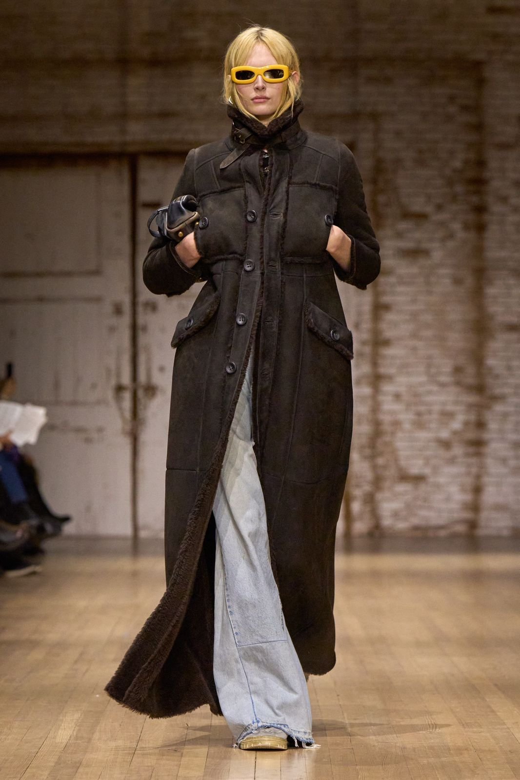 Modelo usa trench coat preto com calça jeans com bolsas tendência do inverno
