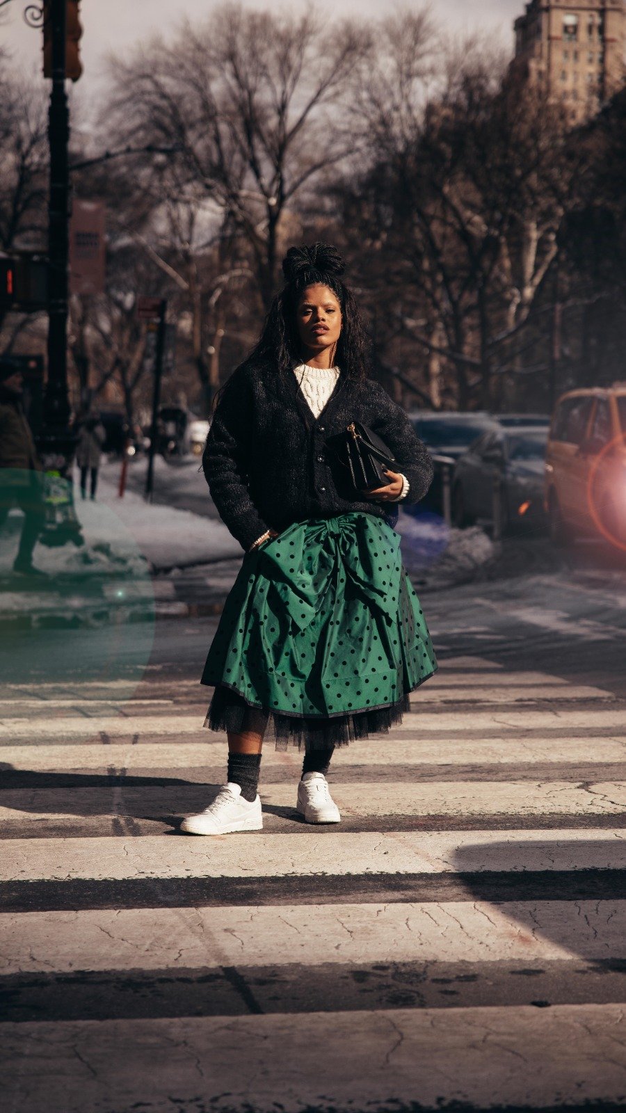 Josy Ramos caminhando em rua de inverno com bolsa preta, tendência da estação. Ela usa casaco e saia verde.

