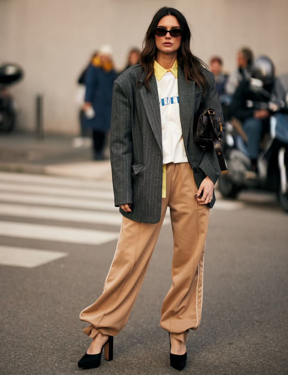 Mulher com blazer cinza e calças largas bege andando na rua, representando peça estilosa.