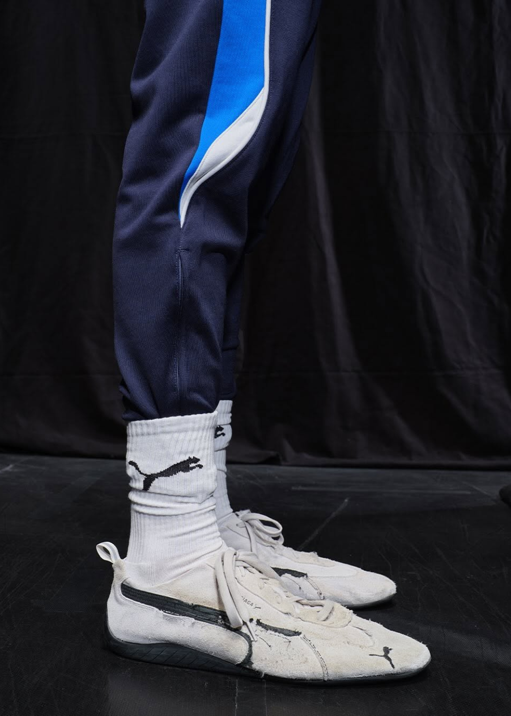Calça azul com detalhe azul claro, meias brancas e tênis de collab estilosa em tom claro com detalhes pretos.