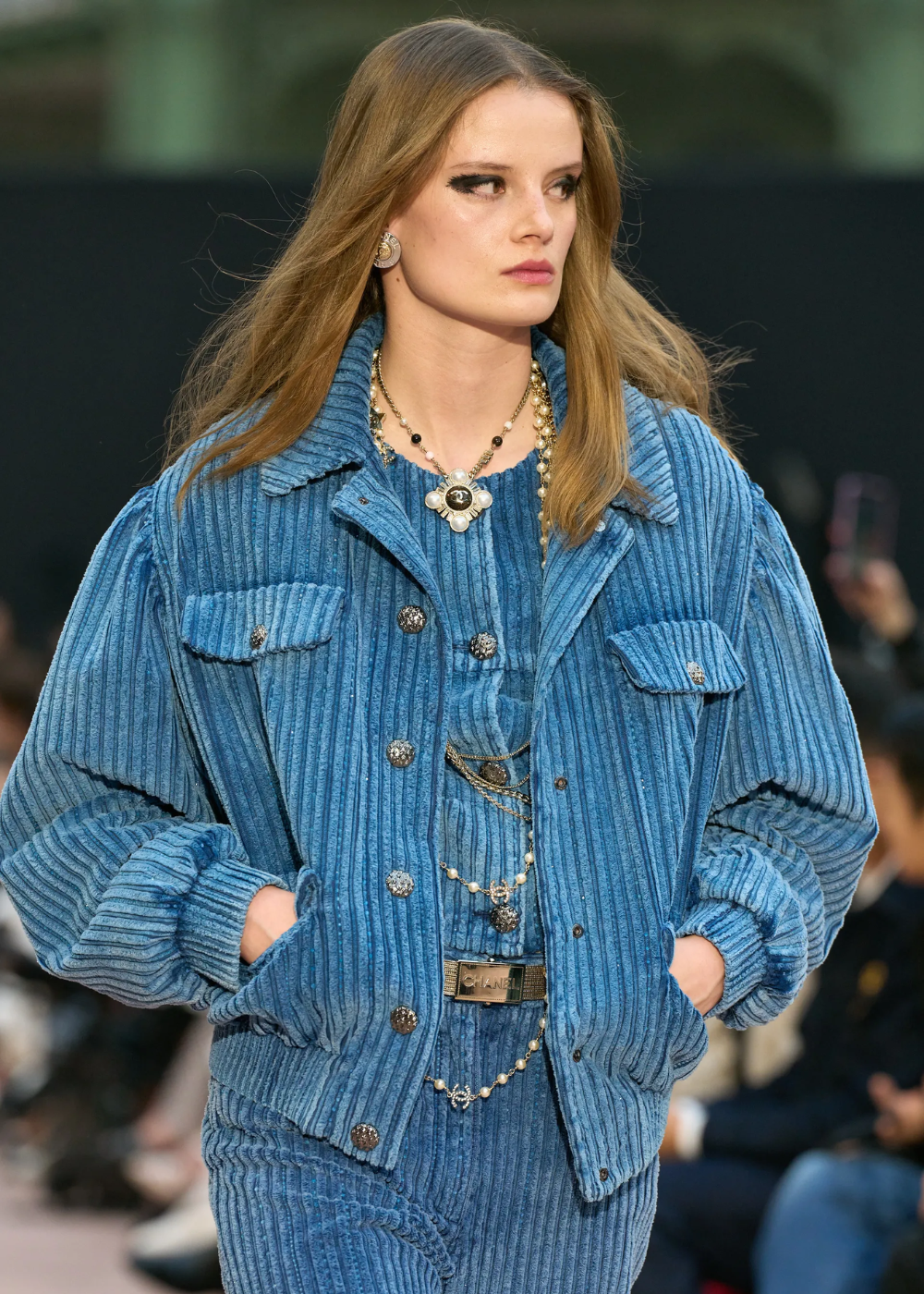 Desfile de moda com pessoa usando jaqueta azul e colar de pérolas elegante.