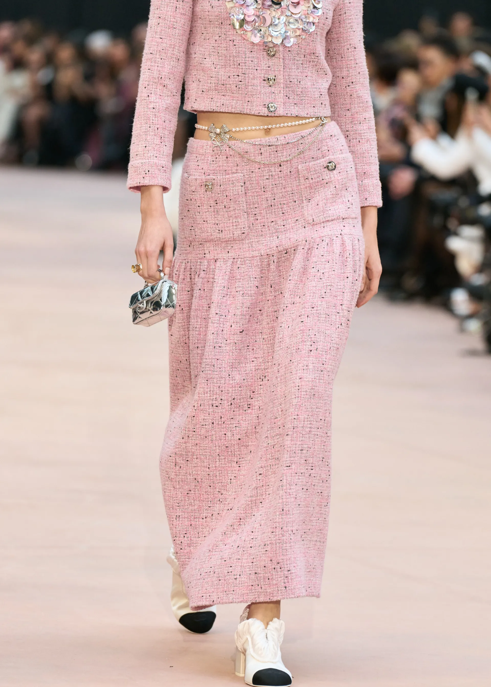 Modelo usando roupa rosa texturizada, bolsa metálica e cinto de pérolas.