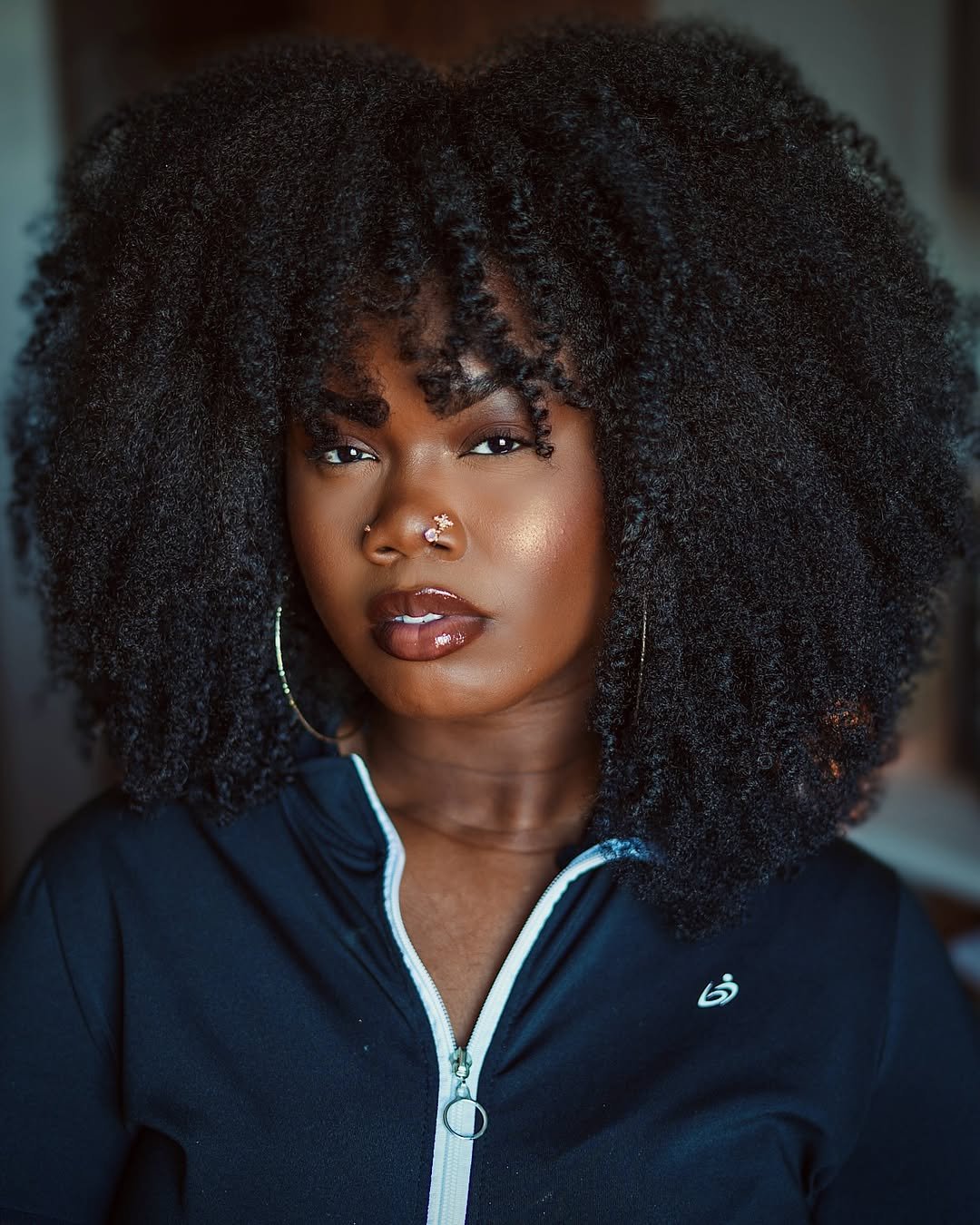 Mulher com cortes de cabelo crespo e cacheado volumoso, estilo natural, usa jaqueta preta com zíper.