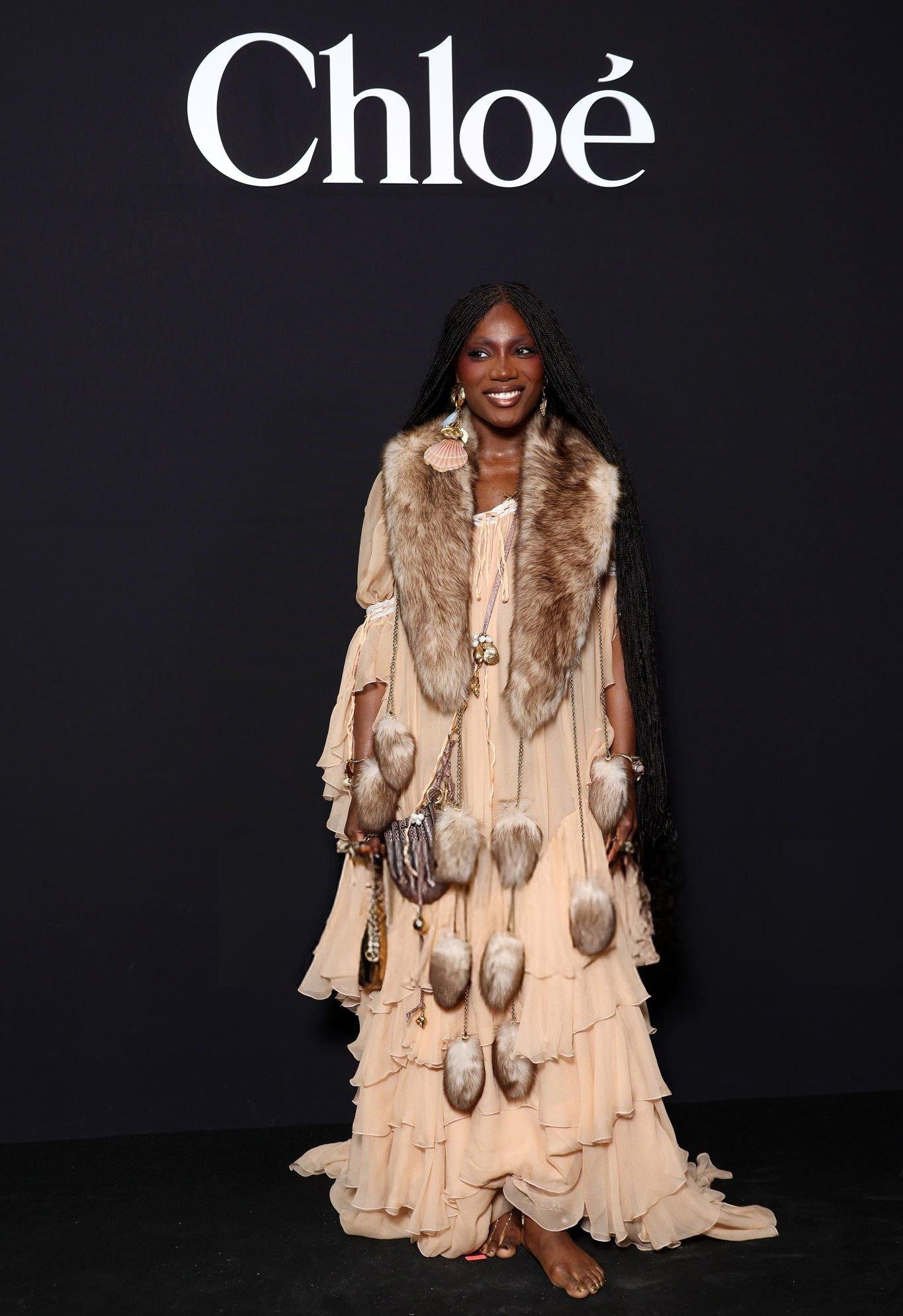 Pessoa em vestido bege com detalhes em pele e acessórios de conchas. Looks da Doechii