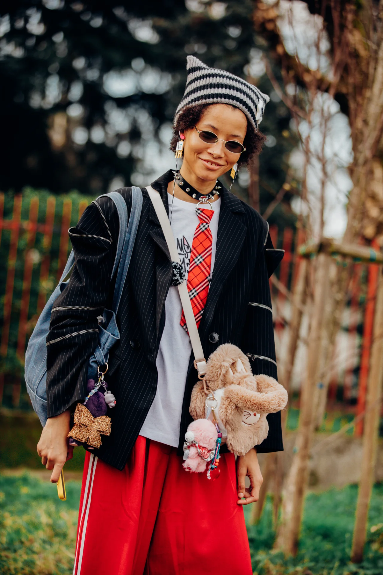 Pessoa com gorro listrado, óculos escuros e bolsa de pelúcia, usando diversos acessórios de moda vibrantes.