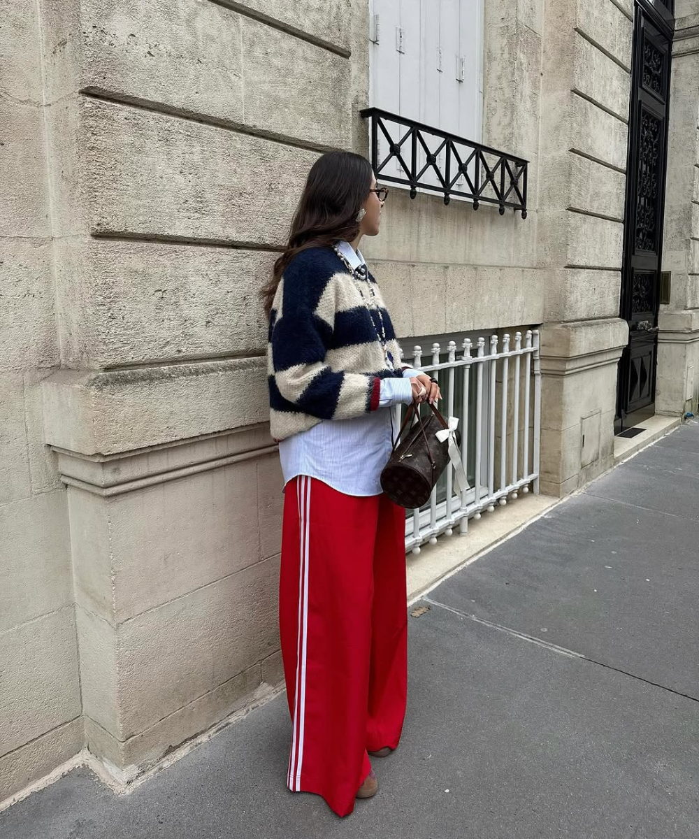 Pessoa com suéter listrado e calça pantalona vermelha, segurando bolsa marrom na rua. Ideias de looks com calça pantalona para o inverno,