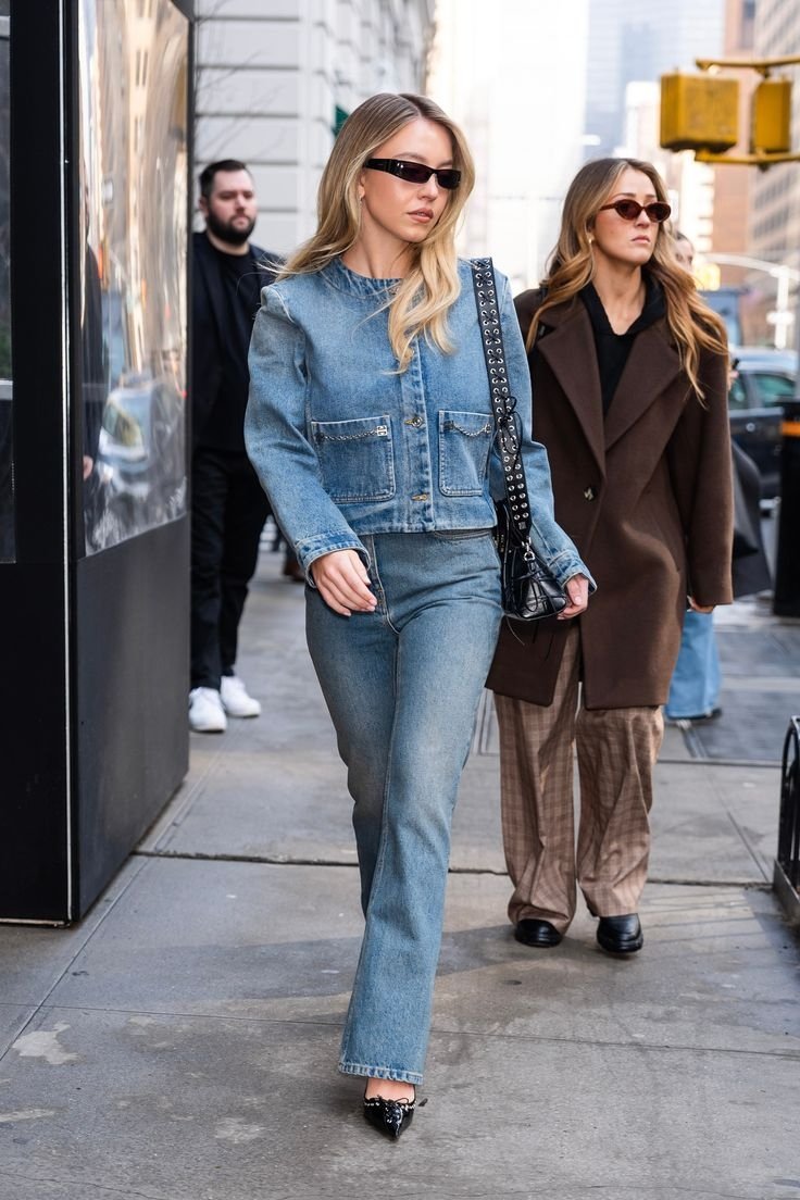 Duas mulheres caminhando em uma calçada. Mulher à frente veste jaqueta e calça jeans. Looks de inverno.
