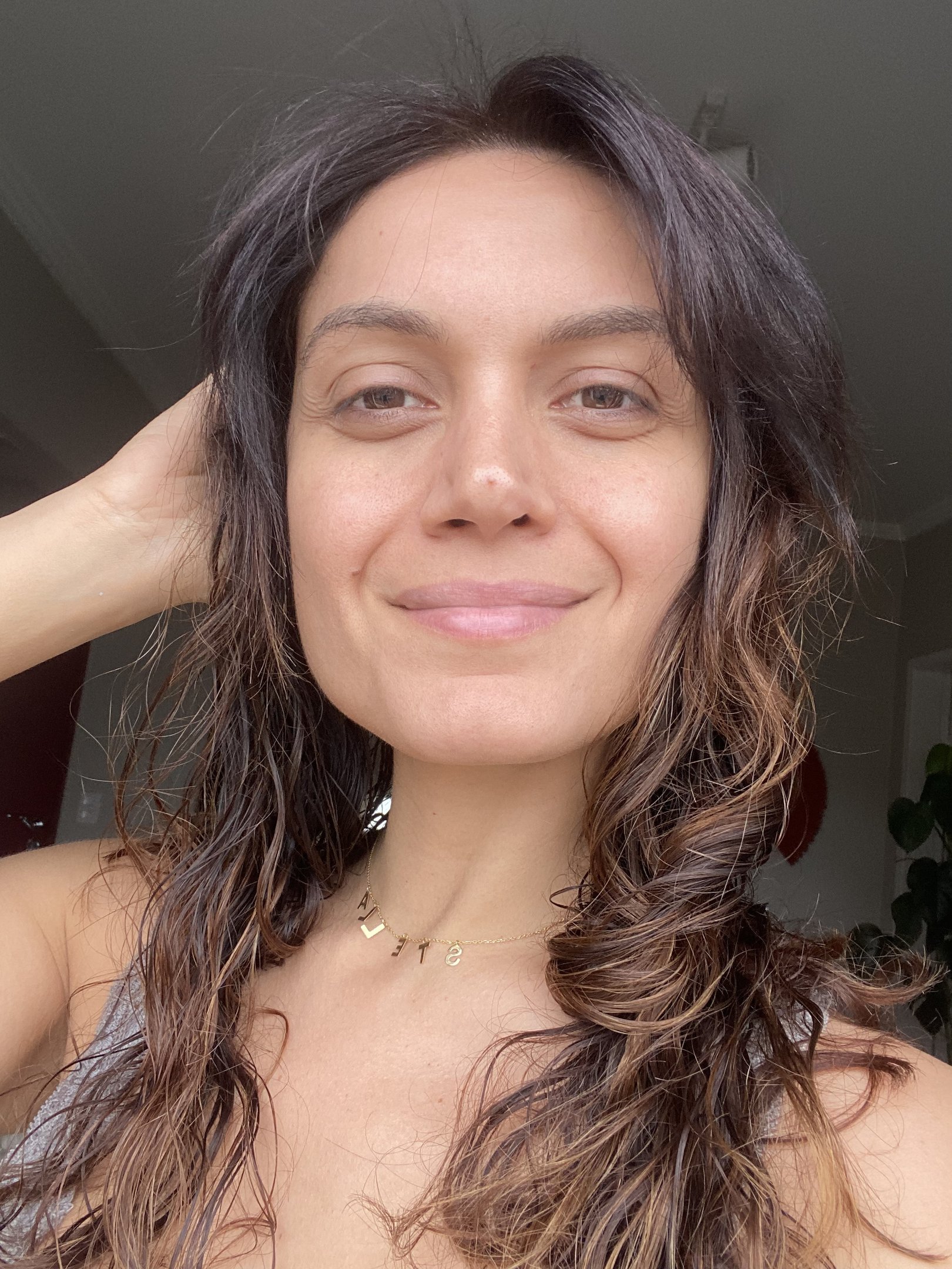 Pessoa com cabelo ondulado, levemente sorrindo, usando colar dourado. após usar máscara de argila da benefit