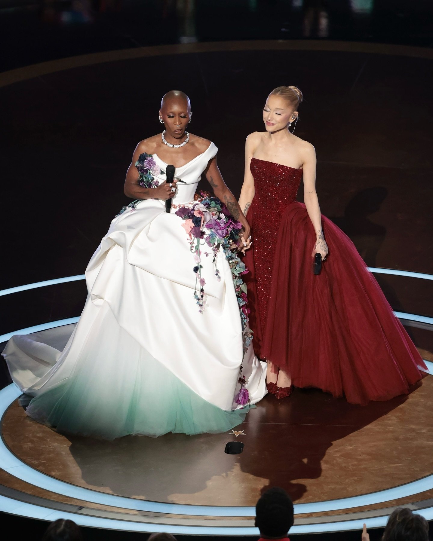 Duas pessoas elegantes de mãos dadas com microfones durante apresentação, simbolizando momentos marcantes do Oscar 2025.